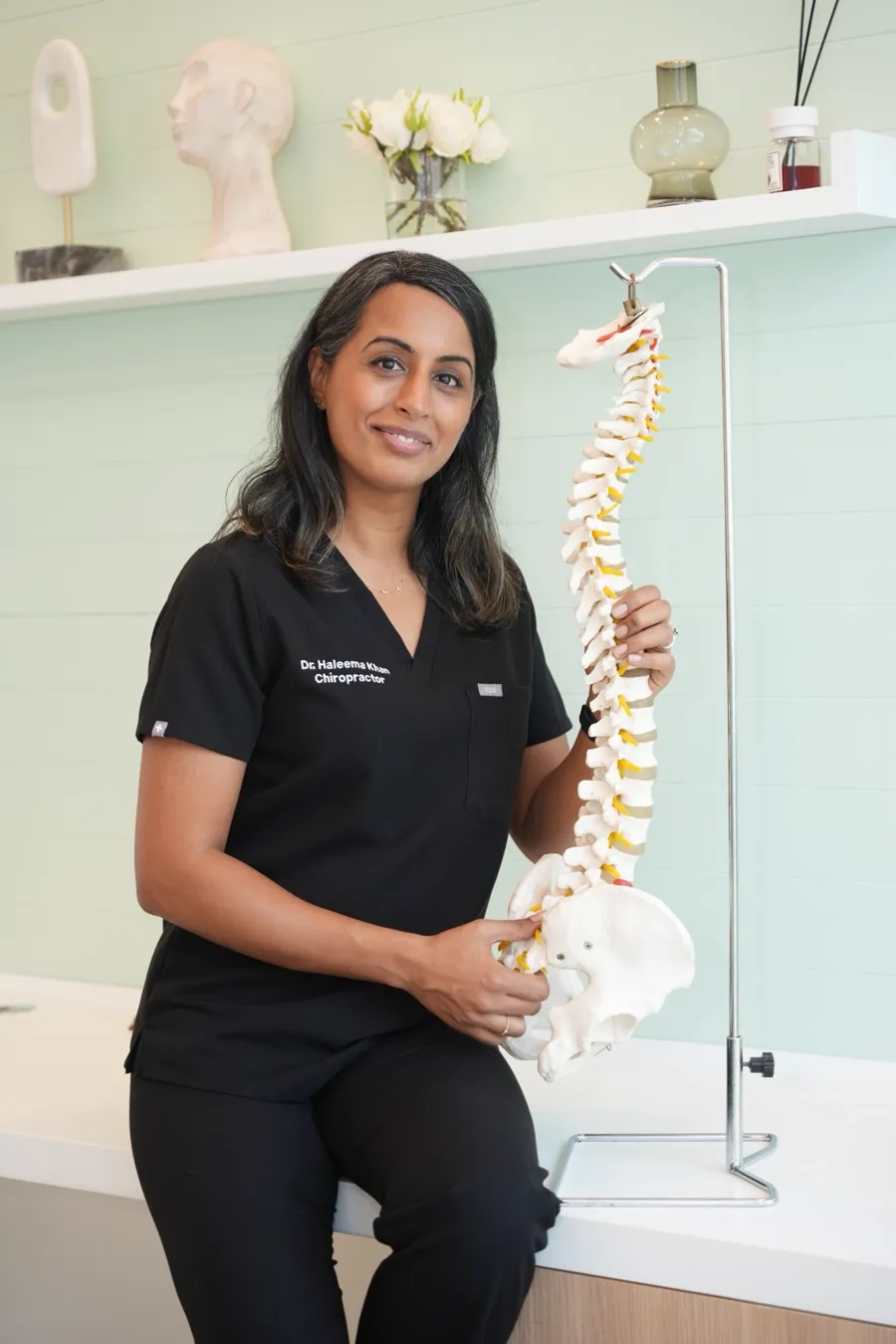 Dr. Haleema Khan in the clinic, holding a model of the human spine